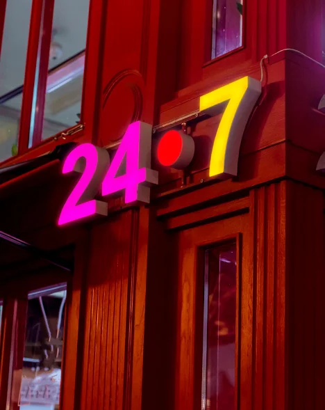 Cifre luminose 24/7 fucsia e gialle su una facciata in legno, esempio d'uso delle pellicole traslucide Avery Dennison Translucent, foto Avery Dennison