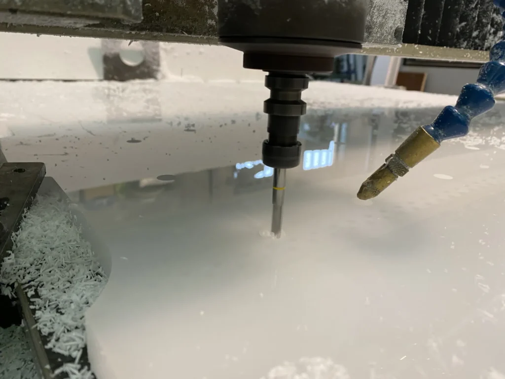 La fresa a controllo numerico che taglia una lastra di plexiglas bianco, con il getto di raffreddamento