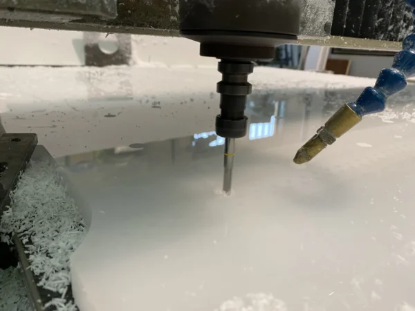 La fresa a controllo numerico che taglia una lastra di plexiglas bianco, con il getto di raffreddamento