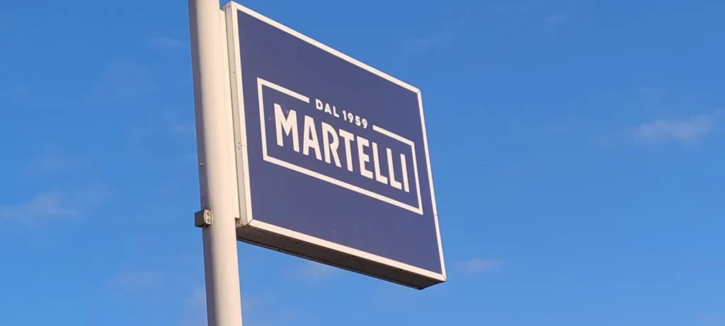 Insegna a cassonetto bifacciale Martelli dal 1969, stagliata contro il cielo azzurro