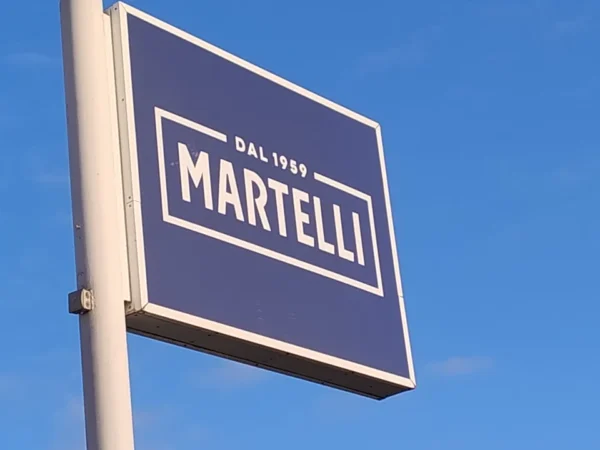 Insegna a cassonetto bifacciale Martelli dal 1969, stagliata contro il cielo azzurro