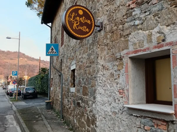Insegna luminosa tonda a cassonetto dell'Antica Rivetta, montata su una parete in pietra