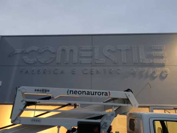 Lettere singole in alluminio dell'insegna Comelstile appena montate sul capannone, dal cestello della piattaforma neonaurora