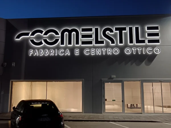 Insegna Comelstile accesa sulla facciata del capannone di Pozzuolo del Friuli, con la riga Fabbrica e centro ottico