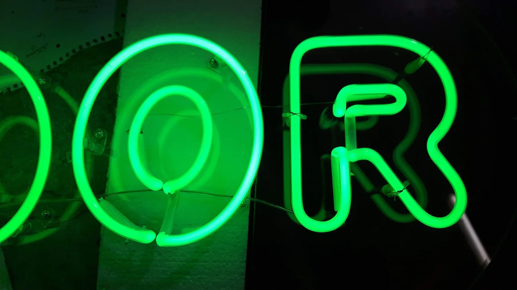 Lettere O e R al neon verde acceso, dettaglio ravvicinato del tubo sagomato