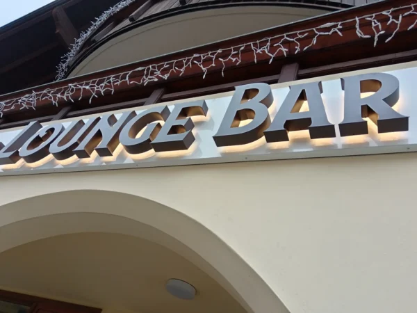 Insegna a lettere singole "Lounge Bar" a luce riflessa, illuminata sul cornicione di un edificio