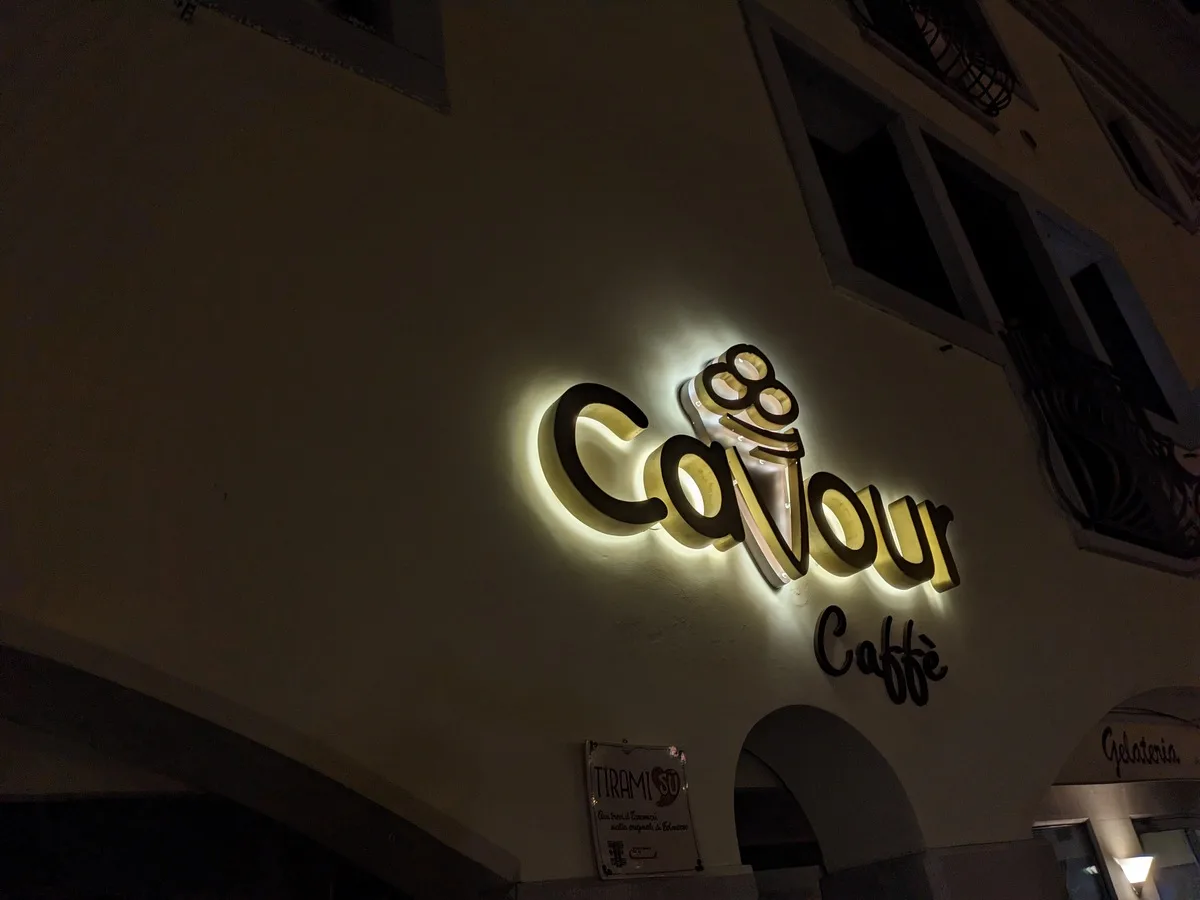 Lettere singole Cavour Caffè retroilluminate di notte sulla facciata, sopra l'ingresso della gelateria