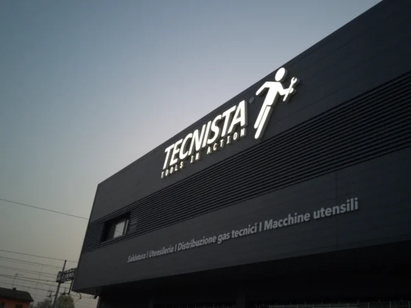 Insegna luminosa Tecnista, tools in action, illuminata sulla facciata scura dell%27edificio al tramonto