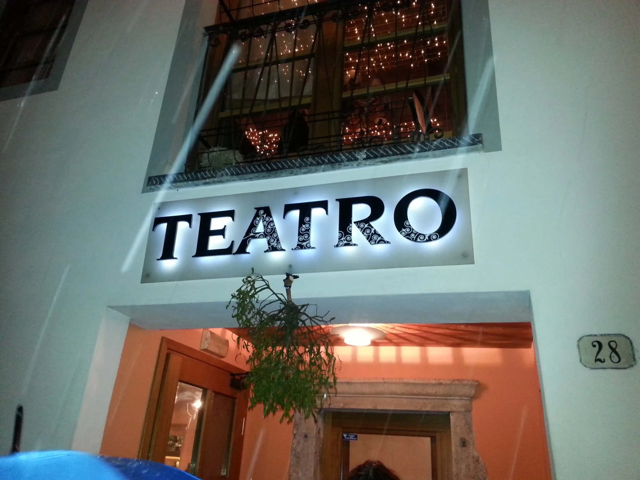 Insegna TEATRO a lettere singole nere su pannello chiaro, luce riflessa accesa al crepuscolo sulla facciata