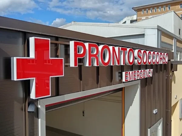 Croce rossa luminosa e lettere Pronto Soccorso Emergency viste di scorcio sull'ingresso dell'ospedale di Tolmezzo