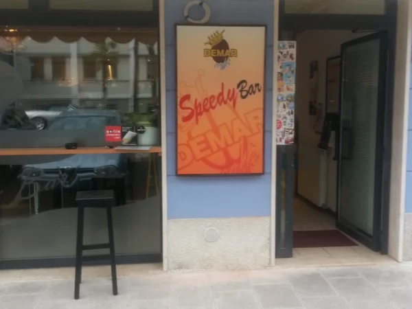 Cassonetto luminoso verticale dello Speedy Bar col logo Demar caff&egrave;, accanto all'ingresso del bar a Gorizia