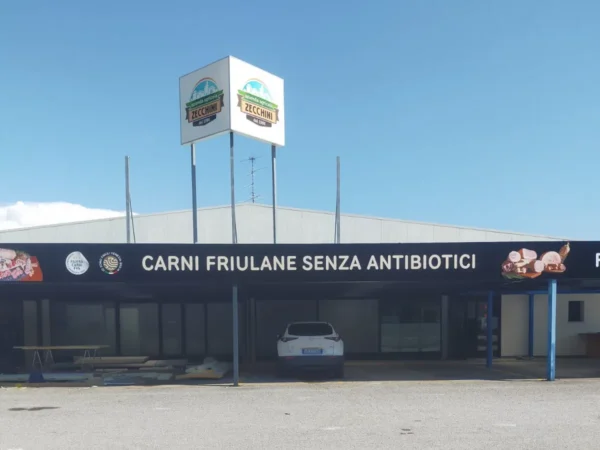 I due cassonetti luminosi col logo Zecchini in cima al palo, sopra la fascia &laquo;Carni friulane senza antibiotici&raquo;