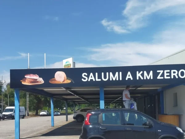 Il lato della tettoia con la scritta &laquo;Salumi a km zero&raquo; e le foto di prosciutto e salame