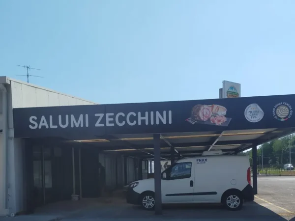 Il lato della tettoia con la scritta &laquo;Salumi Zecchini&raquo; e i marchi della filiera friulana