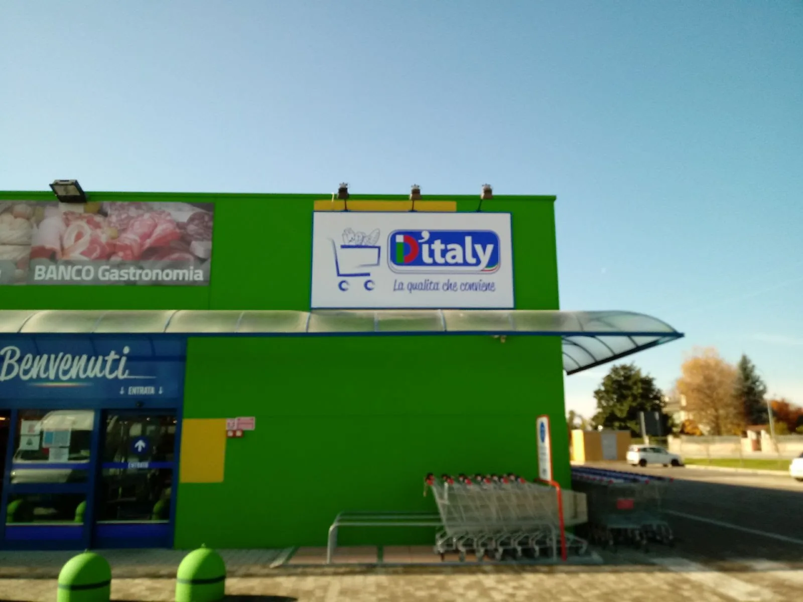 Facciata verde del supermercato D'italy a Udine con l'insegna a pannello e i faretti sopra l'ingresso
