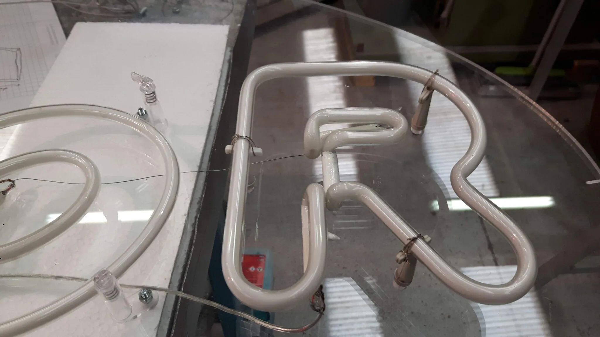 Lettera R in tubo neon spento, bianco, fissata con graffette al piano di lavoro in vetro