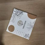 Copertina bianca del listino della SPA Terra Mater di Arta Terme, con le foglie disegnate a mano e i cerchi color sabbia