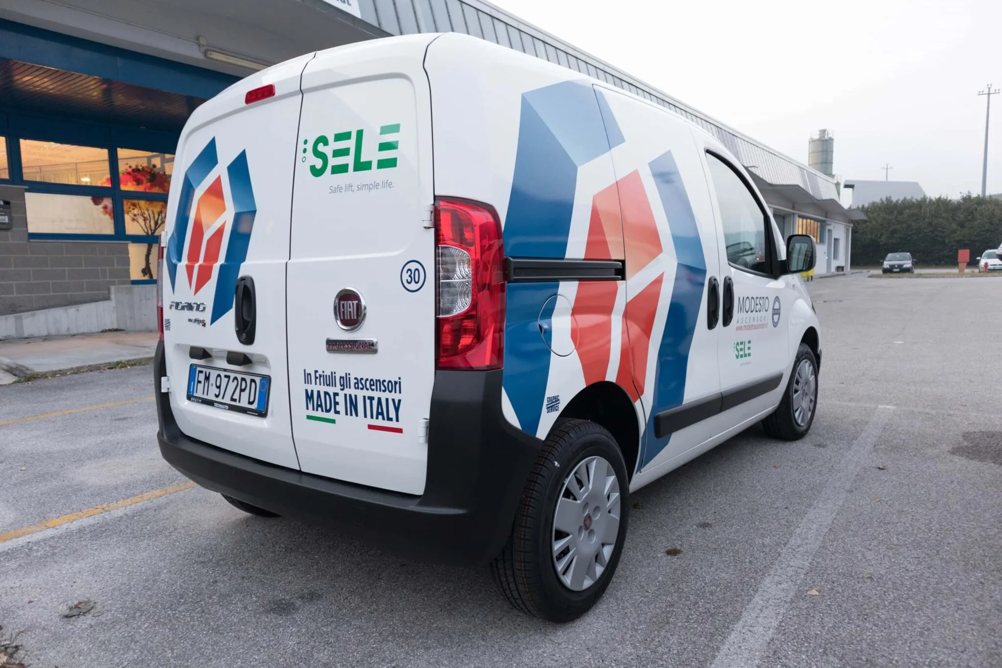 Furgone Modesto Ascensori visto da dietro con grafica a esagoni rossi e blu, logo Sele e scritta Made in Italy