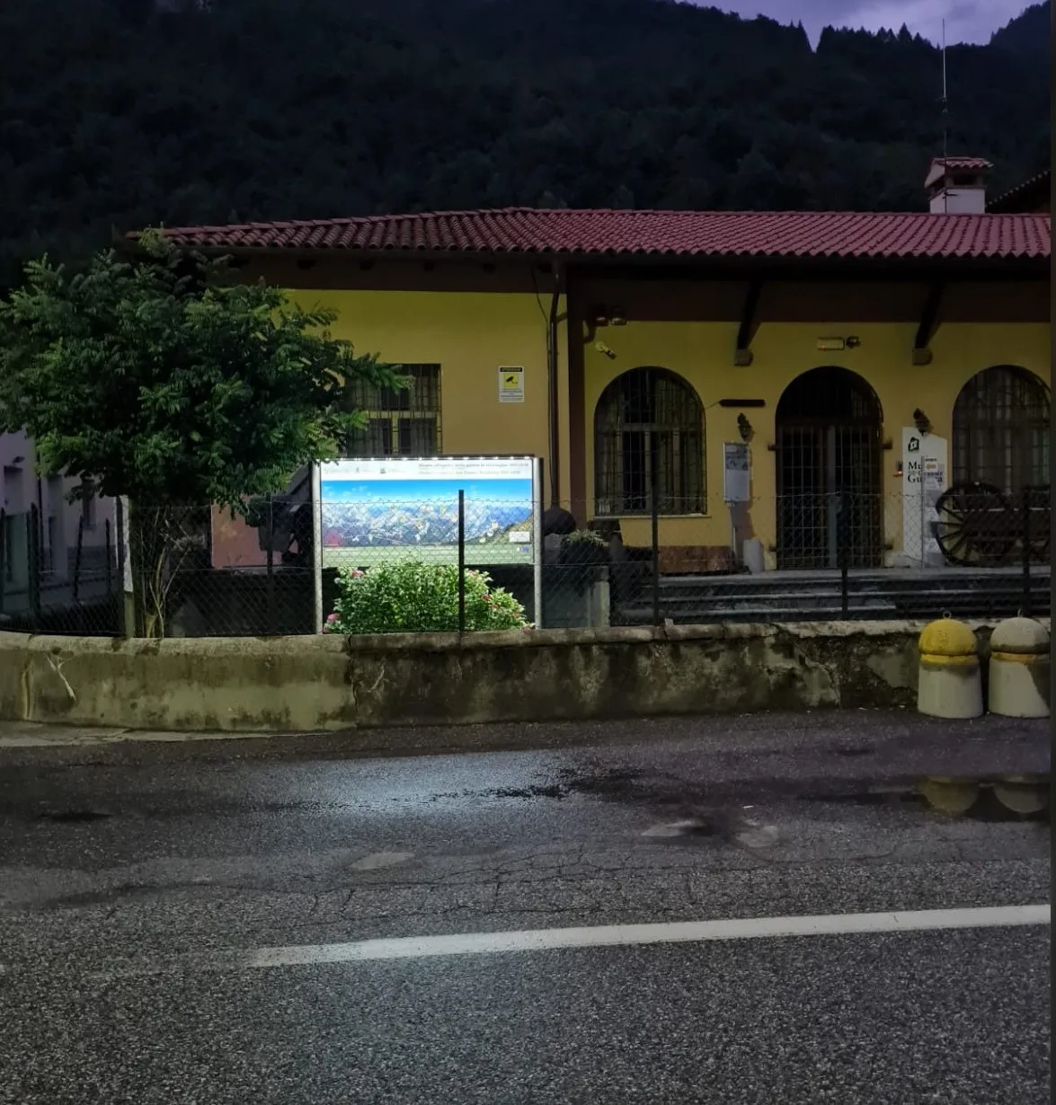 Bacheca luminosa del museo vista dalla strada al crepuscolo, davanti all'edificio giallo di Timau