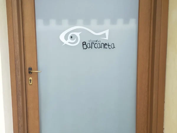 Porta d'ingresso della Trattoria Barcaneta con il vetro sabbiato e il logo, sotto il portico