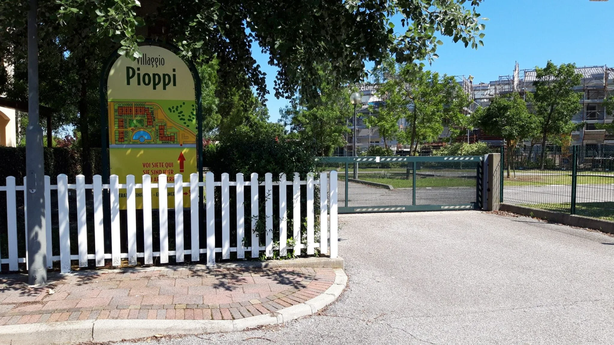 Cartello del Villaggio Pioppi con mappa, davanti alla staccionata bianca e al cancello d'ingresso