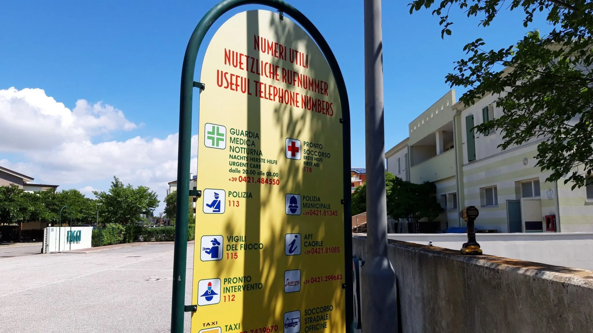 Cartello Numeri utili visto di lato, con pittogrammi e numeri di emergenza stampati