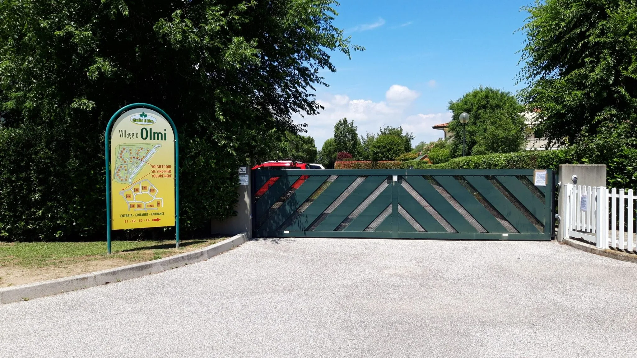 Cartello del Villaggio Olmi con mappa, vicino al cancello verde a doghe oblique