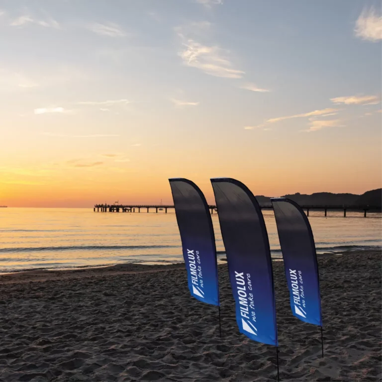 Tre beach flag blu in tessuto LUXtex Easy Flag piantati sulla spiaggia al tramonto, foto Filmolux