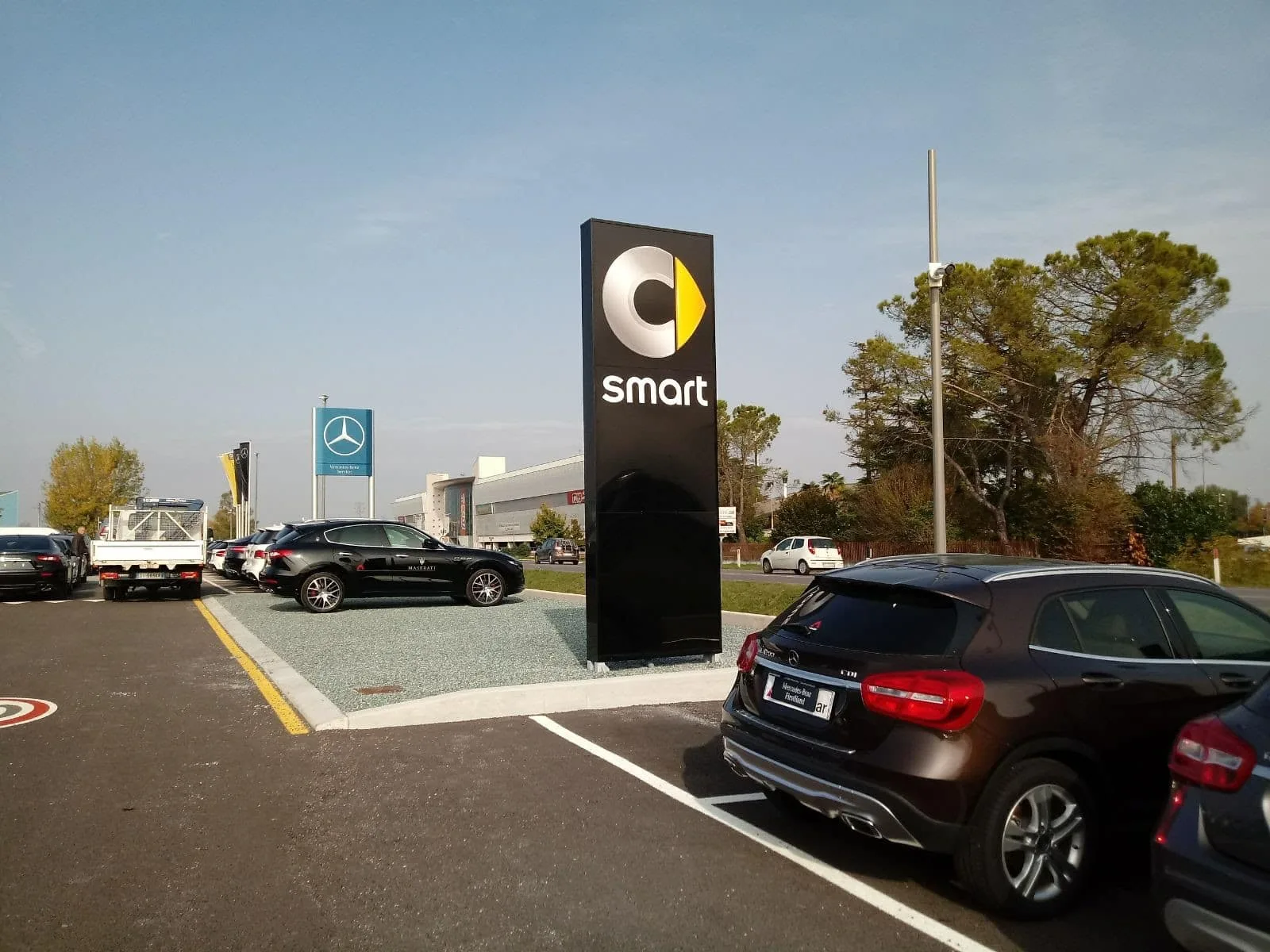Totem nero con logo e scritta smart nel piazzale dell'area Smart di Udine, tra le auto parcheggiate