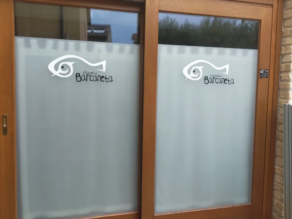 Vetrofanie sabbiate con il pesce del logo Barcaneta sulle vetrate della trattoria a Marano Lagunare