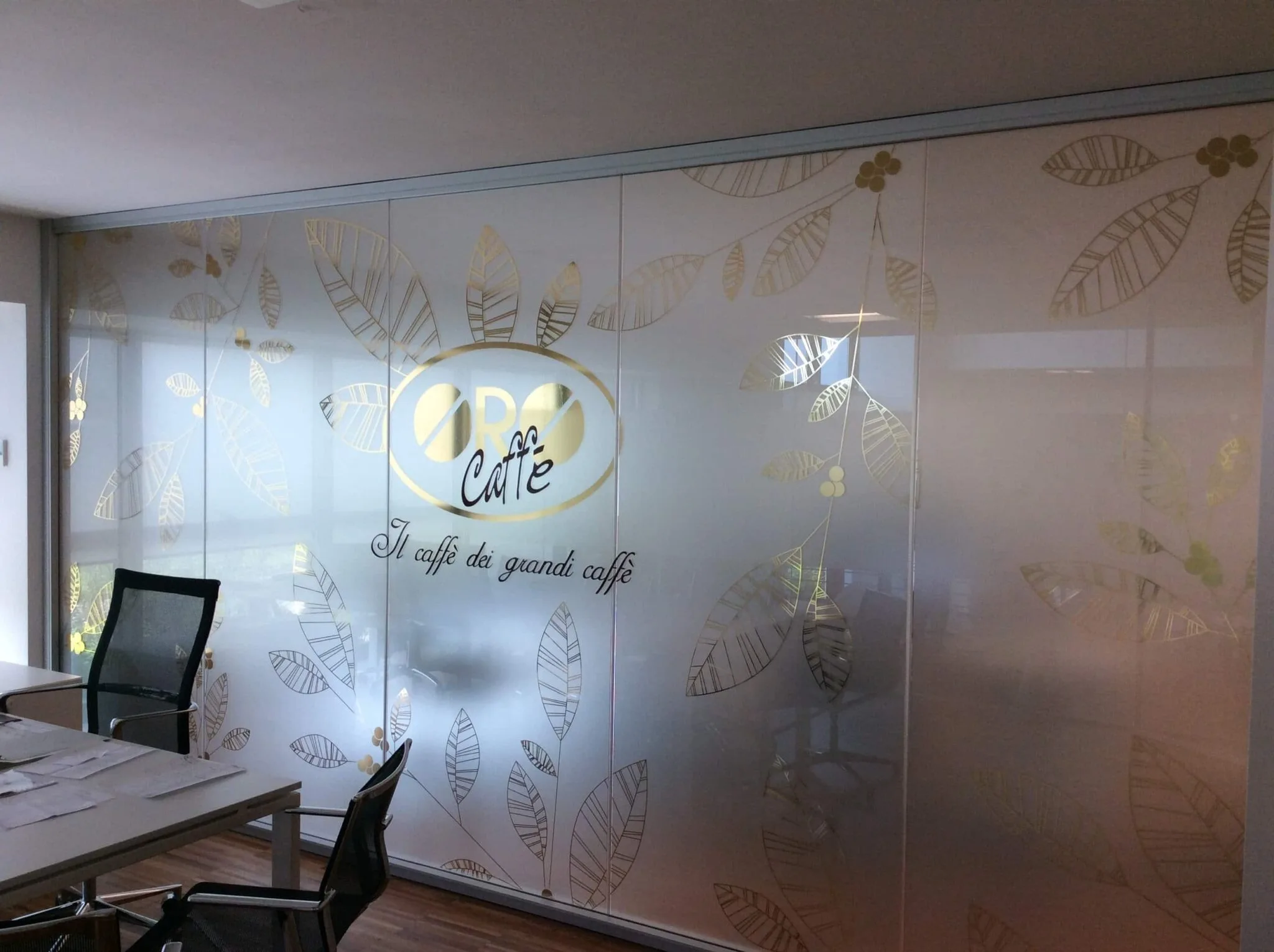 Grande vetrata sabbiata con logo ovale in oro a specchio, foglie decorative e slogan scritto a mano