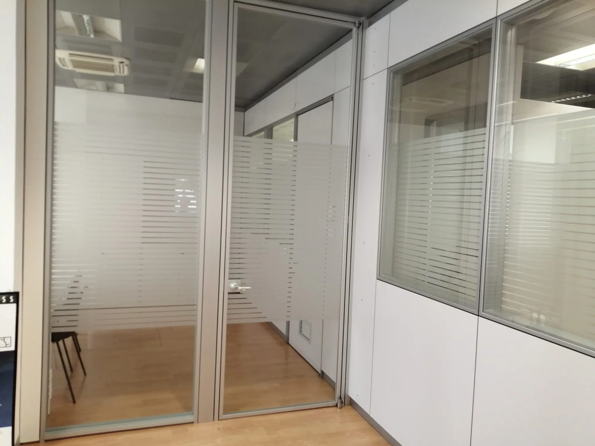 Porta e pareti divisorie in vetro con strisce di pellicola sabbiata che schermano la vista nell'ufficio