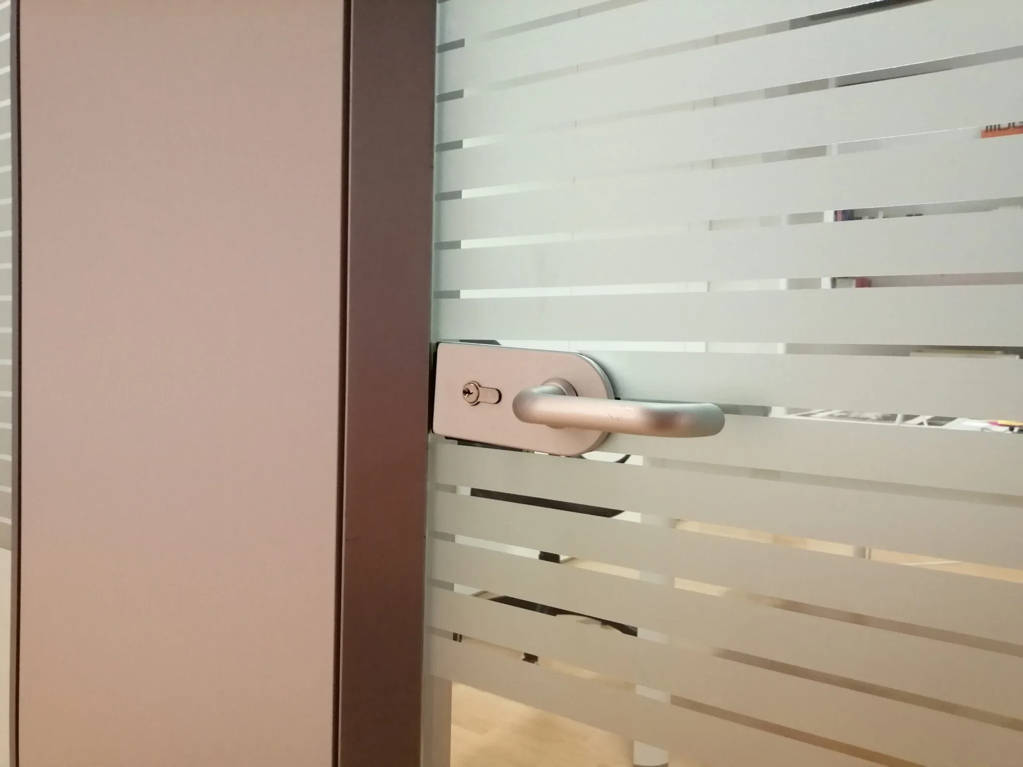 Dettaglio della maniglia su una porta a vetro con pellicola sabbiata a righe di altezze diverse