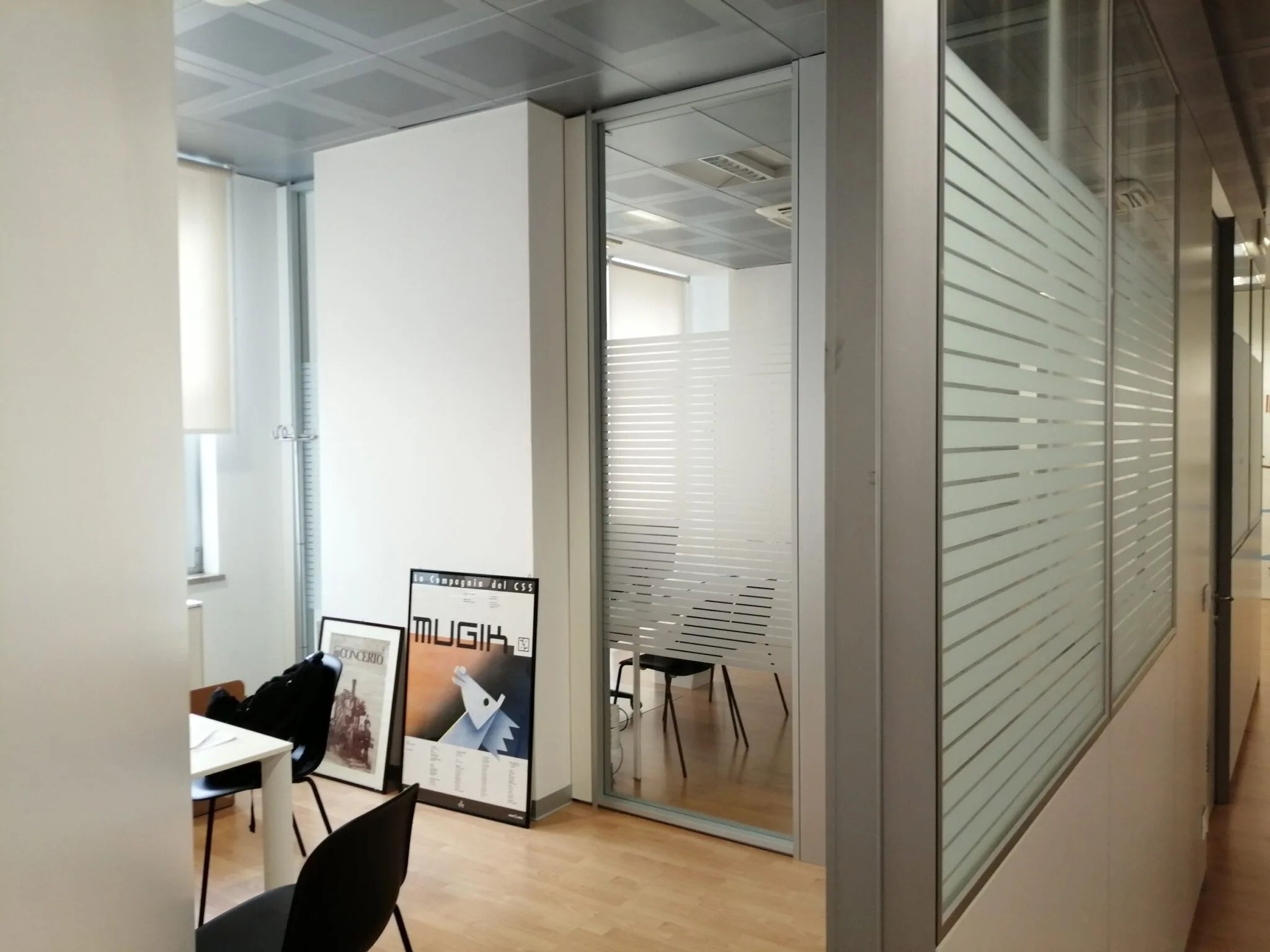 Ufficio con pareti vetrate a righe sabbiate che garantiscono privacy, vista dal corridoio verso la sala riunioni